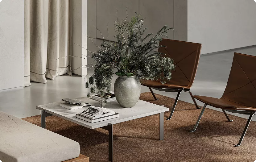 Detailopname van een salontafel met vaas en groen, boeken en stoelen op een vloerkleed in een moderne woonruimte