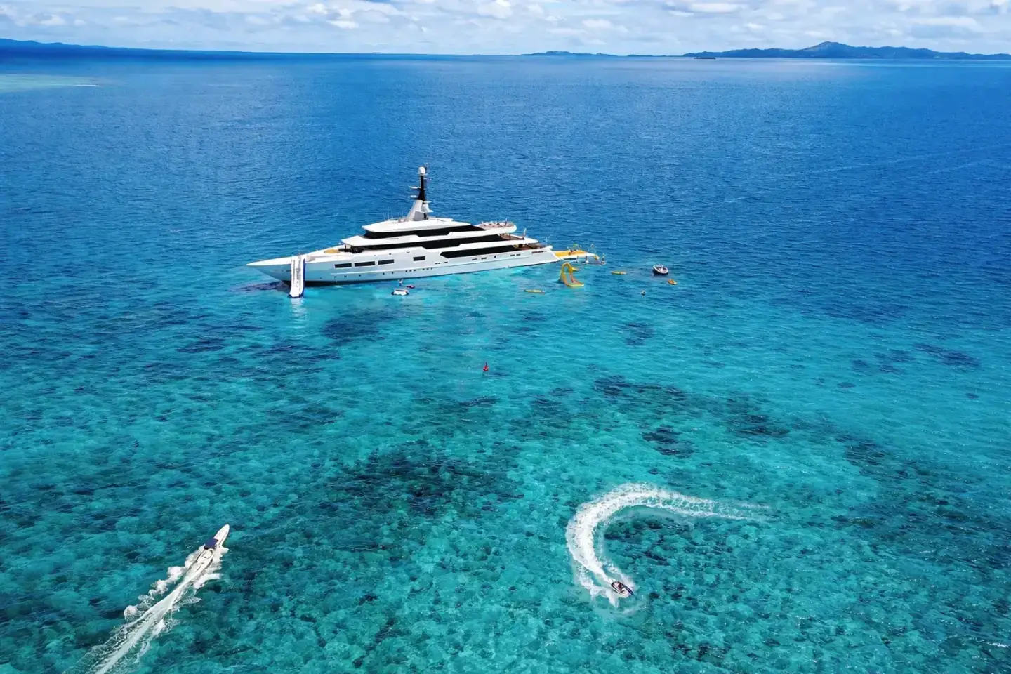 Large superyacht anchored in shallow tropical water with tenders, swimmers, and water activities
