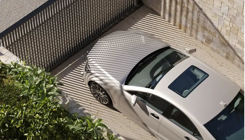 Auto bianca parcheggiata davanti al cancello a lamelle, con le ombre rigate sul vialetto