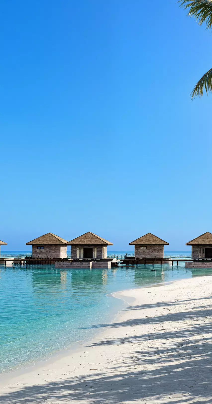 Visualización arquitectónica de villas sobre pilotes frente a una laguna turquesa en calma y una playa de arena blanca vacía bajo un cielo despejado.