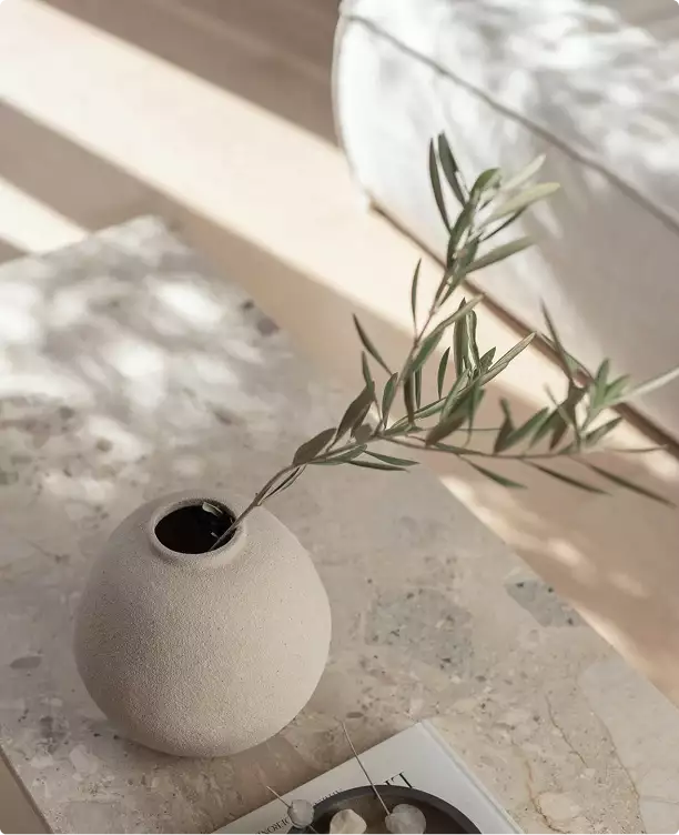 Dettaglio d'arredo della casa in animazione 3D con vaso rotondo e ramo di ulivo su un tavolo in pietra