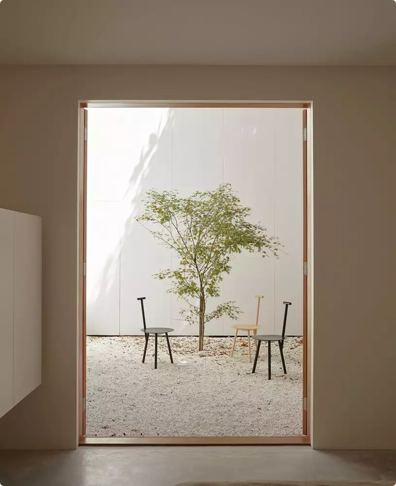 3D-rondleiding langs een binnenplaats met een kleine boom, drie stoelen en wit grind