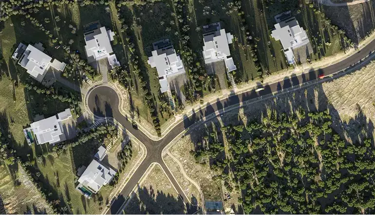 Render de vista aérea de un barrio de villas desde arriba, con carreteras, sombras de árboles y casas modernas