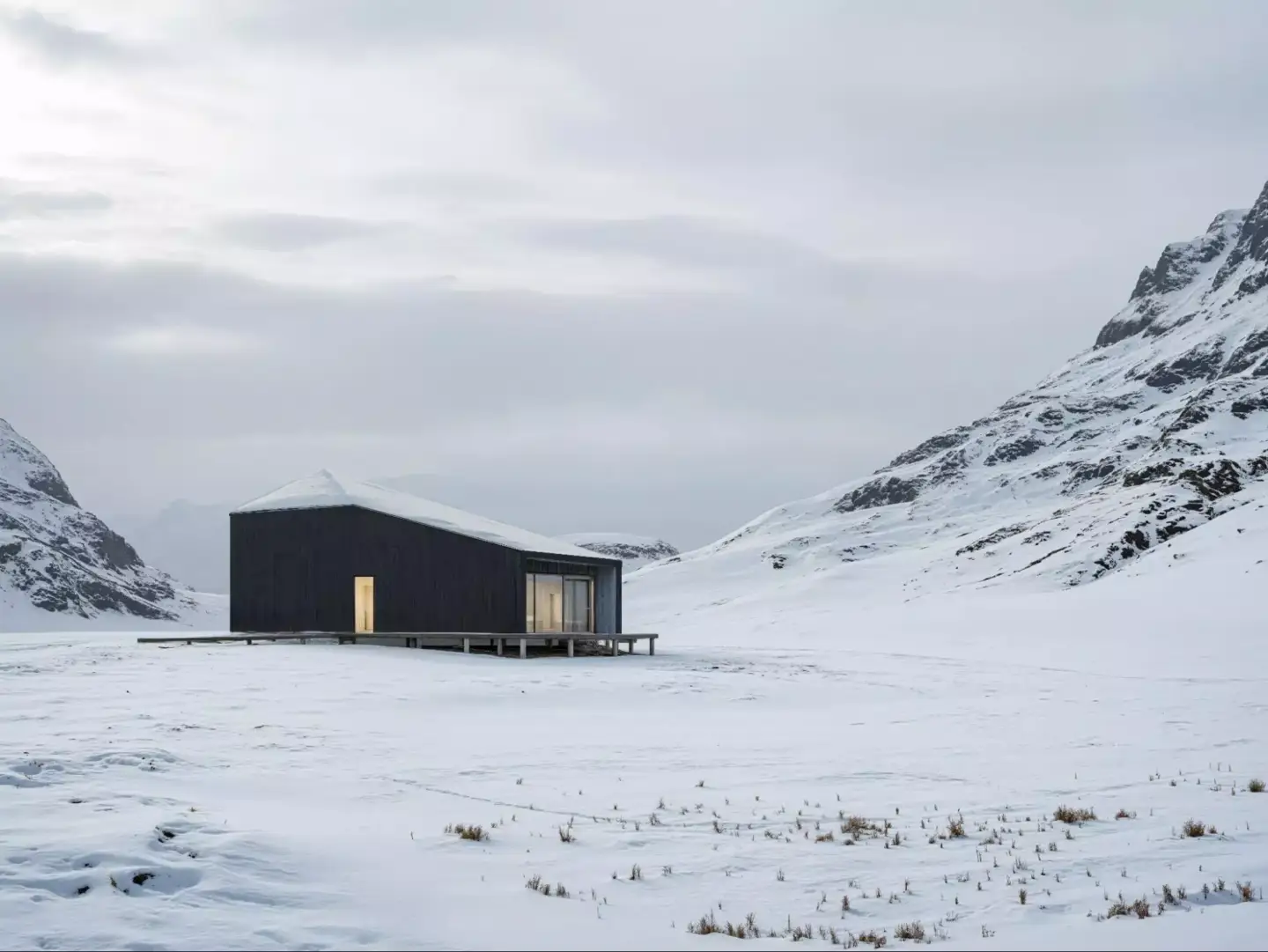 Minimal dark cabin in a snowy mountain valley with glowing windows