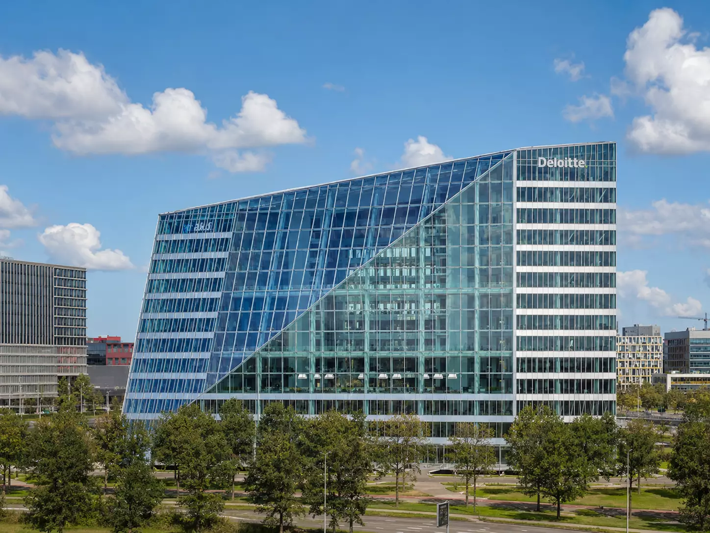 Glass office building with trees and reflective facade under a bright blue sky
