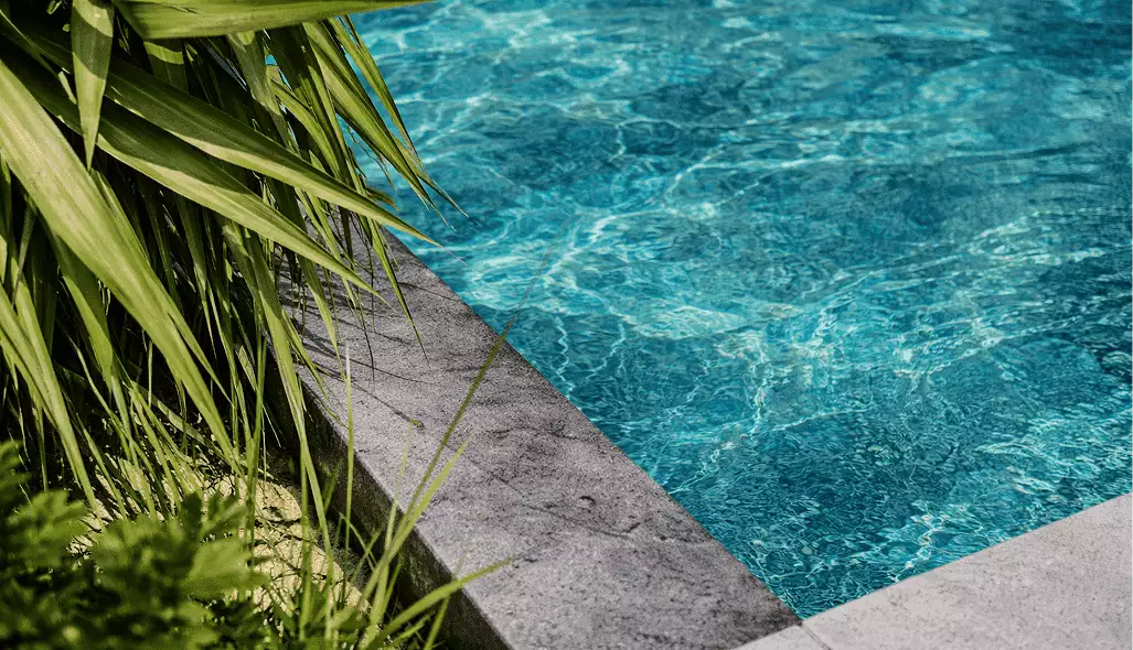 3D-hotelrender bij het zwembad met turquoise water, natuurstenen rand en tropische bladeren