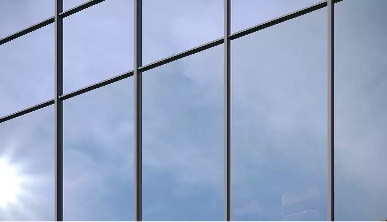 Detalle de fachada de vidrio en renders de rascacielos con montantes oscuros y cielo azul pálido reflejado en los paneles.