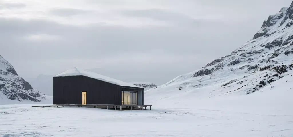Wintervisualisierung einer dunklen Hütte im verschneiten Bergtal mit beleuchtetem Eingang und bedecktem Himmel