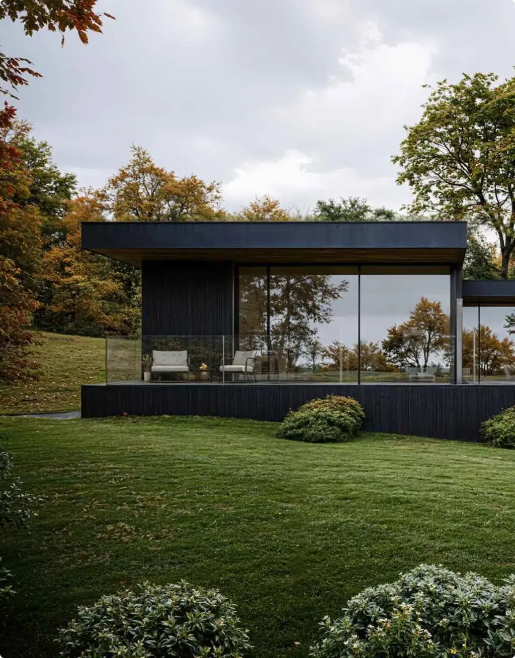 Vastgoedvisualisatie van een zwart modern huis met glazen gevel en herfstgazon