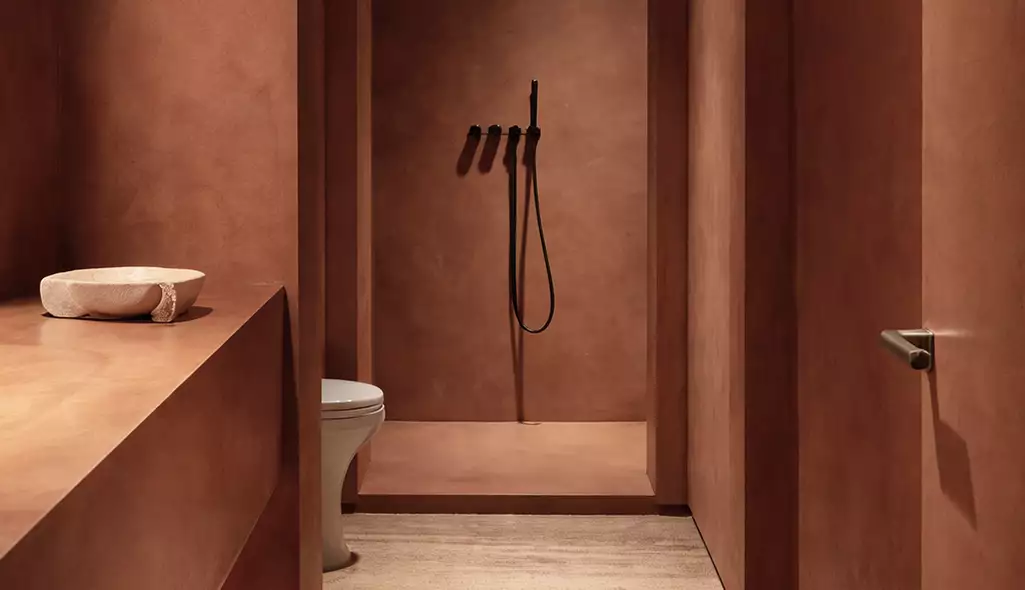 Baño en la visualización del resort, con paredes de arcilla, ducha y lavabo en tonos cálidos