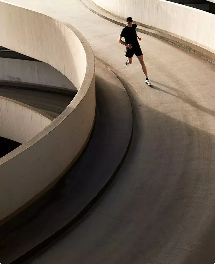 Runner su rampa curva nell'interior design di un centro fitness con architettura in cemento levigato e movimento dinamico