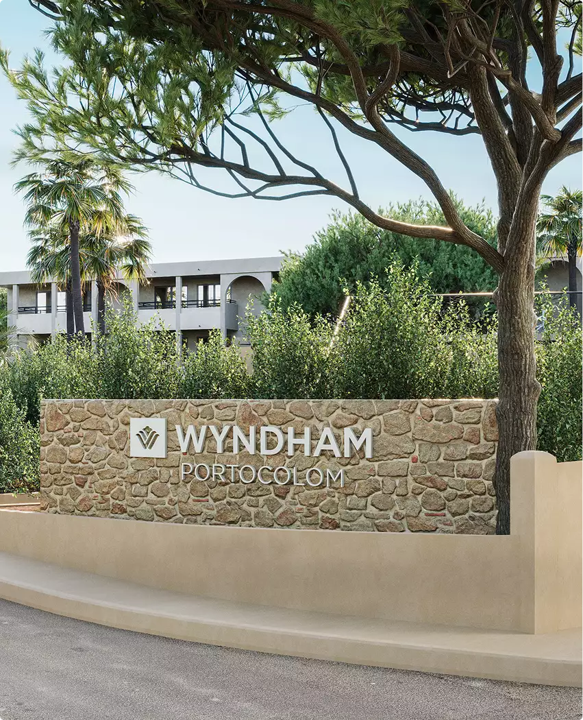 Render 3D de hotel con el cartel de piedra de la entrada, el rótulo Wyndham Portocolom y la vegetación del entorno