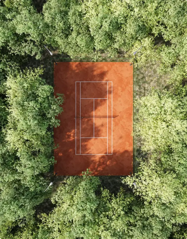 Rendu architectural photoréaliste : court de tennis en terre battue vu du ciel entre des arbres denses
