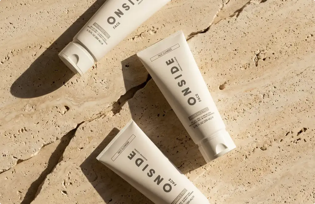 Flat-lay render of three cream skincare tubes on a cracked travertine slab