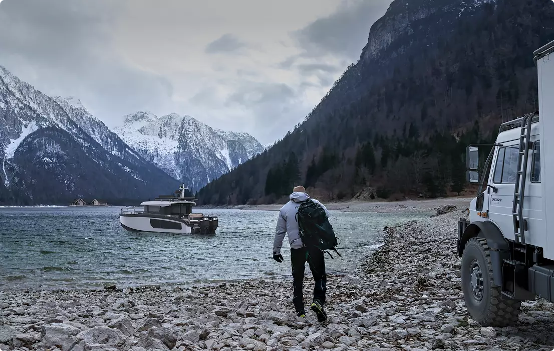 Yacht-Visualisierung eines kleinen Boots auf einem Bergsee mit Wanderer, felsigem Ufer, Expeditionsfahrzeug und schneebedeckten Gipfeln