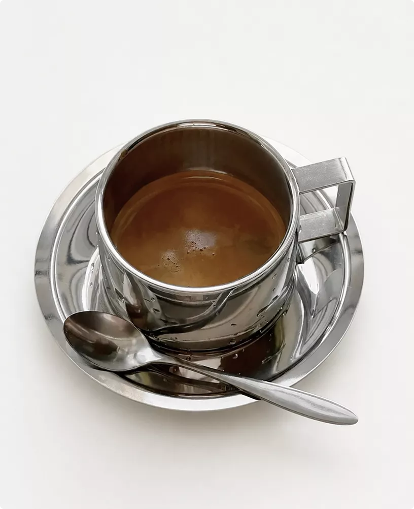Metalen koffiekop op schotel in café-interieur in CGI met lepel op witte achtergrond