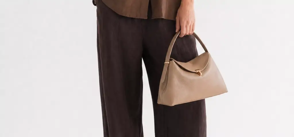 Beige Toteme handbag held with brown outfit against neutral background