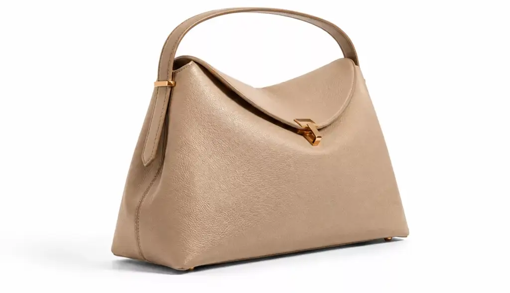 Beige Toteme handbag with curved handle and gold clasp on gray background