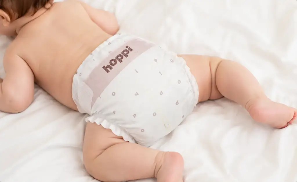 Baby resting on white bedding in a hoppi diaper, baby diaper lifestyle render.