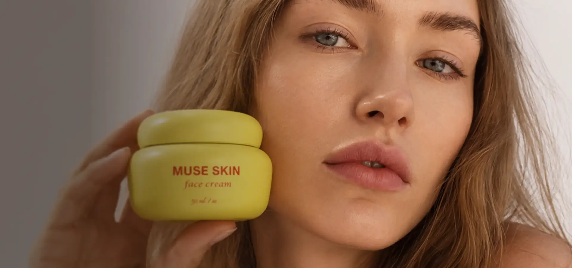 Modella beauty con un barattolo di crema viso giallo vicino alla guancia, visualizzazione di prodotto con AI per un brand skincare.