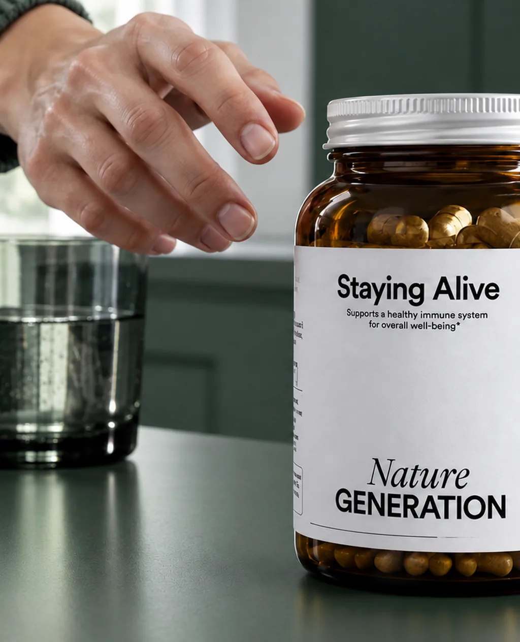 A hand reaching for the Staying Alive bottle, capsules visible through the amber glass