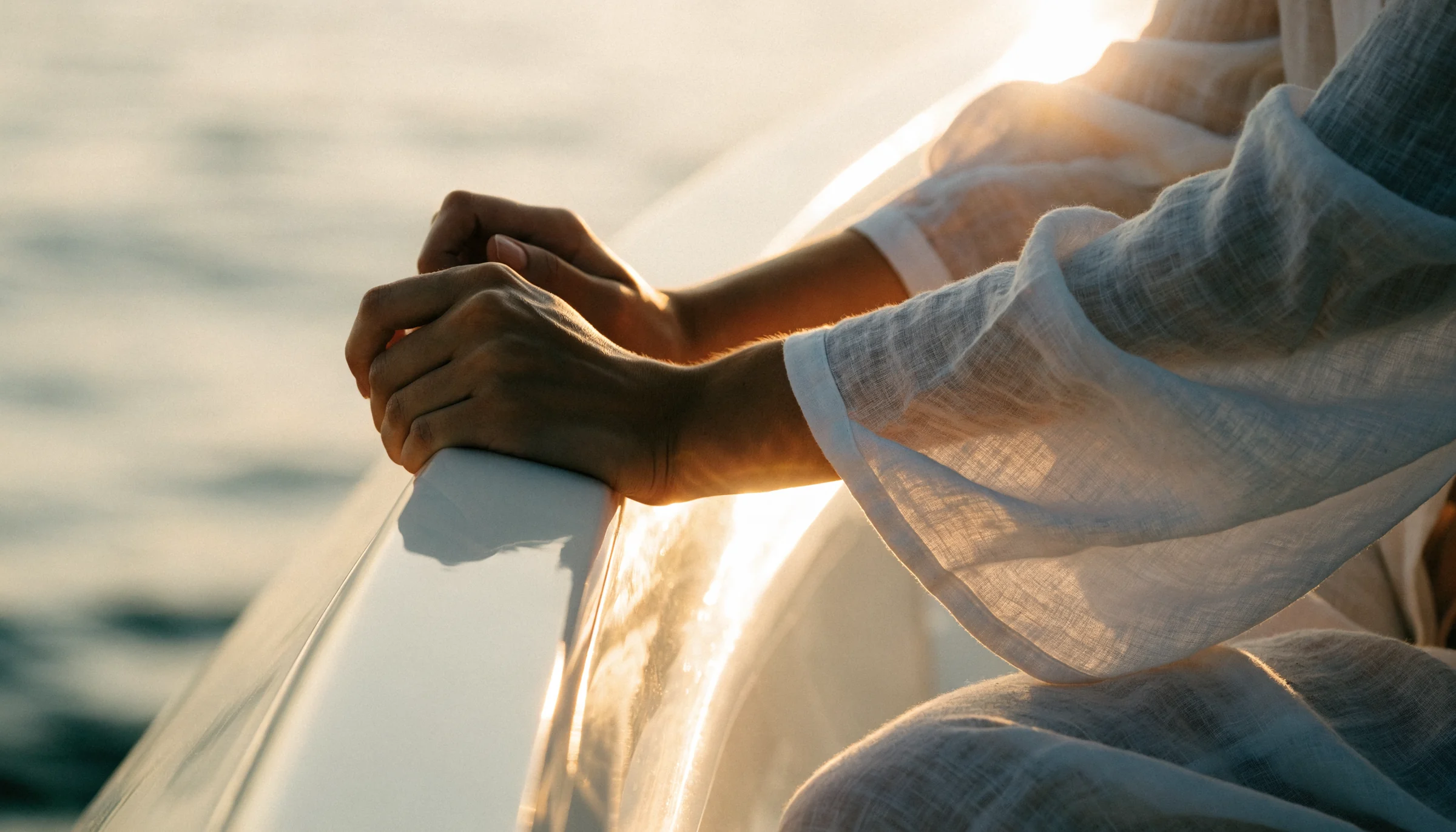 Fotogramma verticale delle mani di una donna appoggiate alla battagliola di uno yacht nella calda luce bassa del sole sul mare