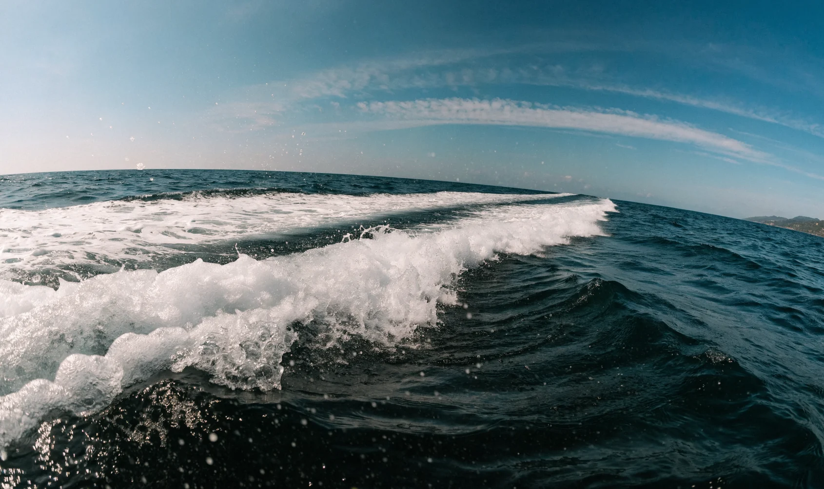 La scia di un motoscafo che curva sull’acqua blu in mare aperto, vista appena sopra la superficie