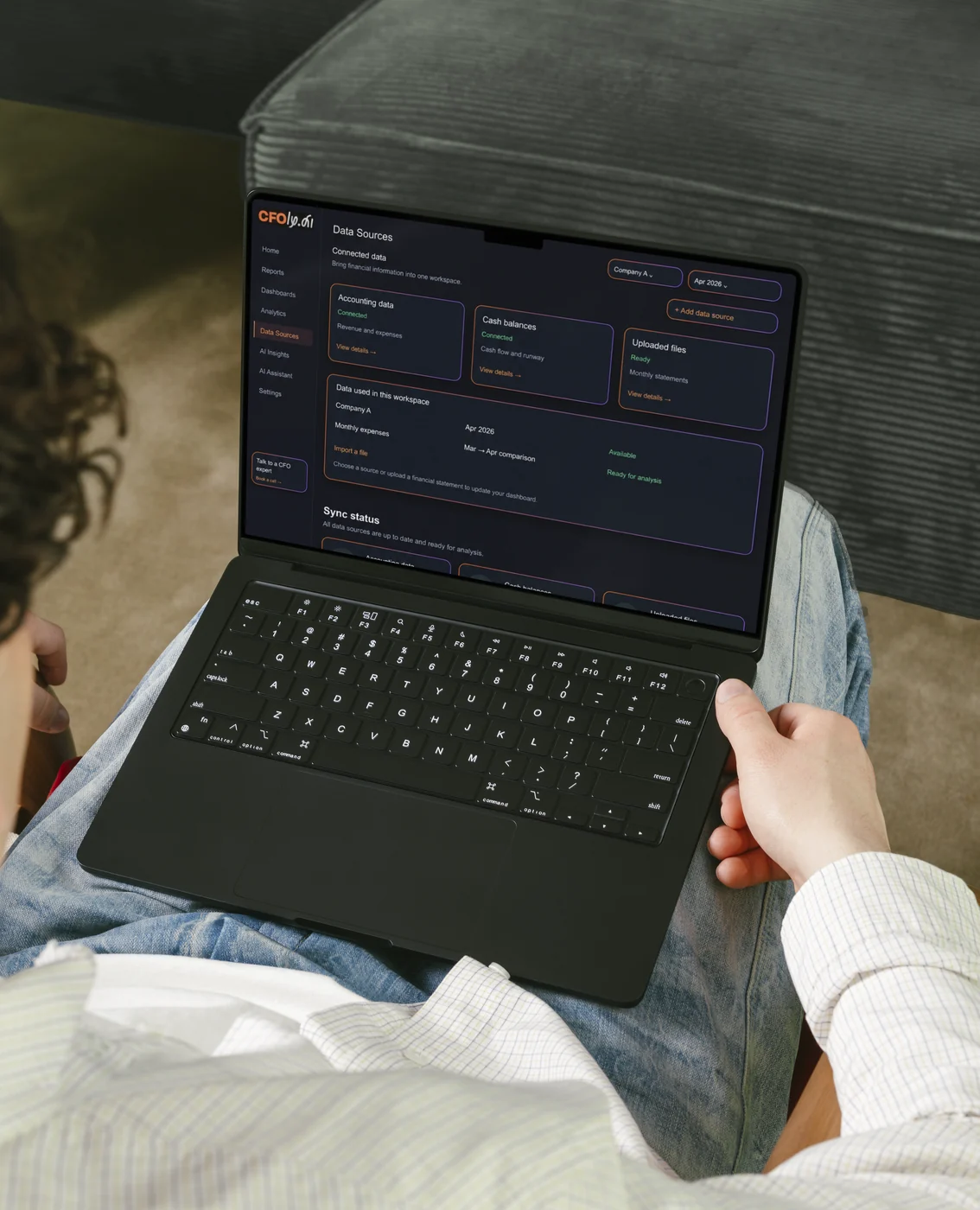 Persoon met een laptop op de knieën, met het scherm met databronnen van een AI-CFO-app op het display