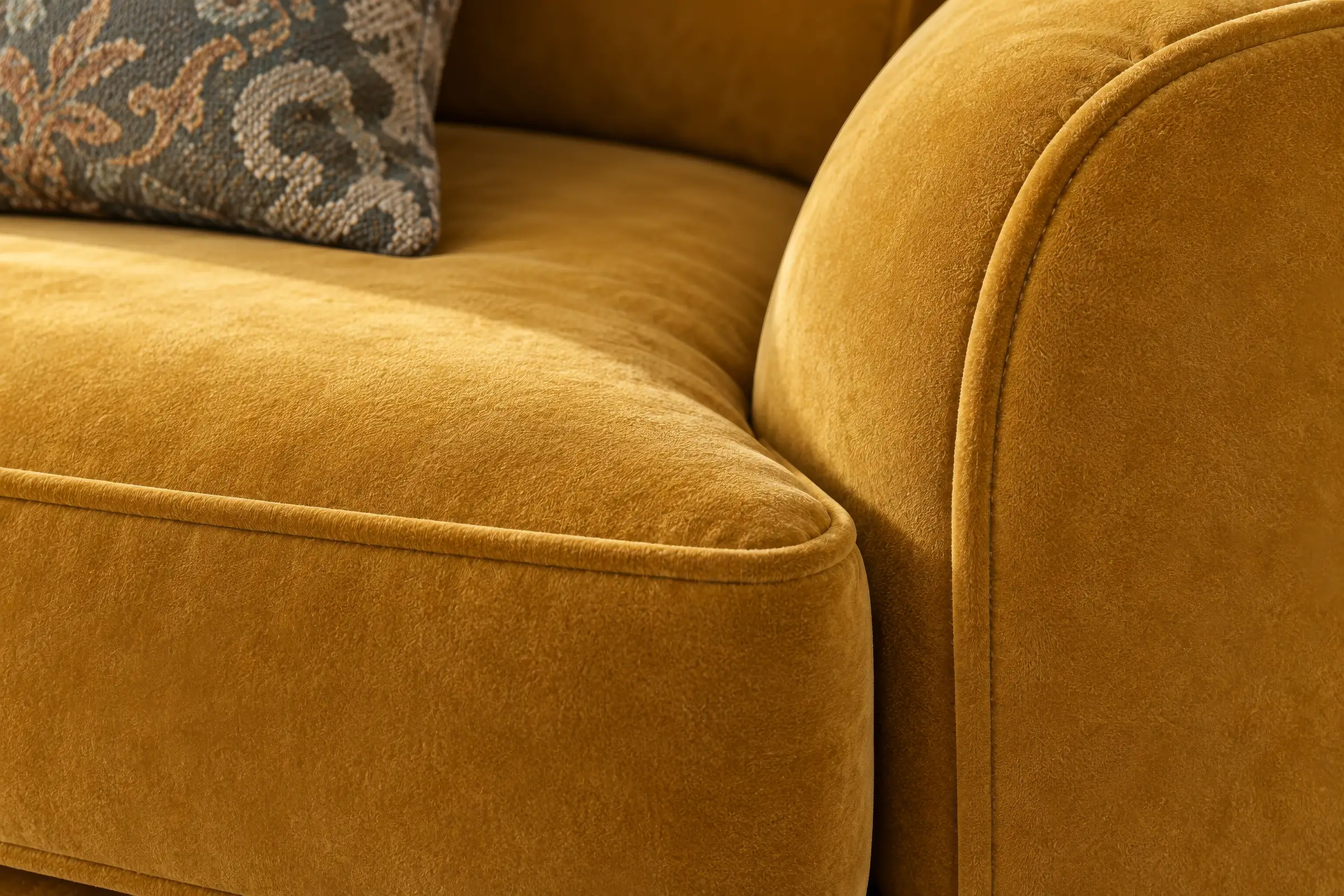 Close-up render of a mustard velvet sofa arm with a patterned cushion