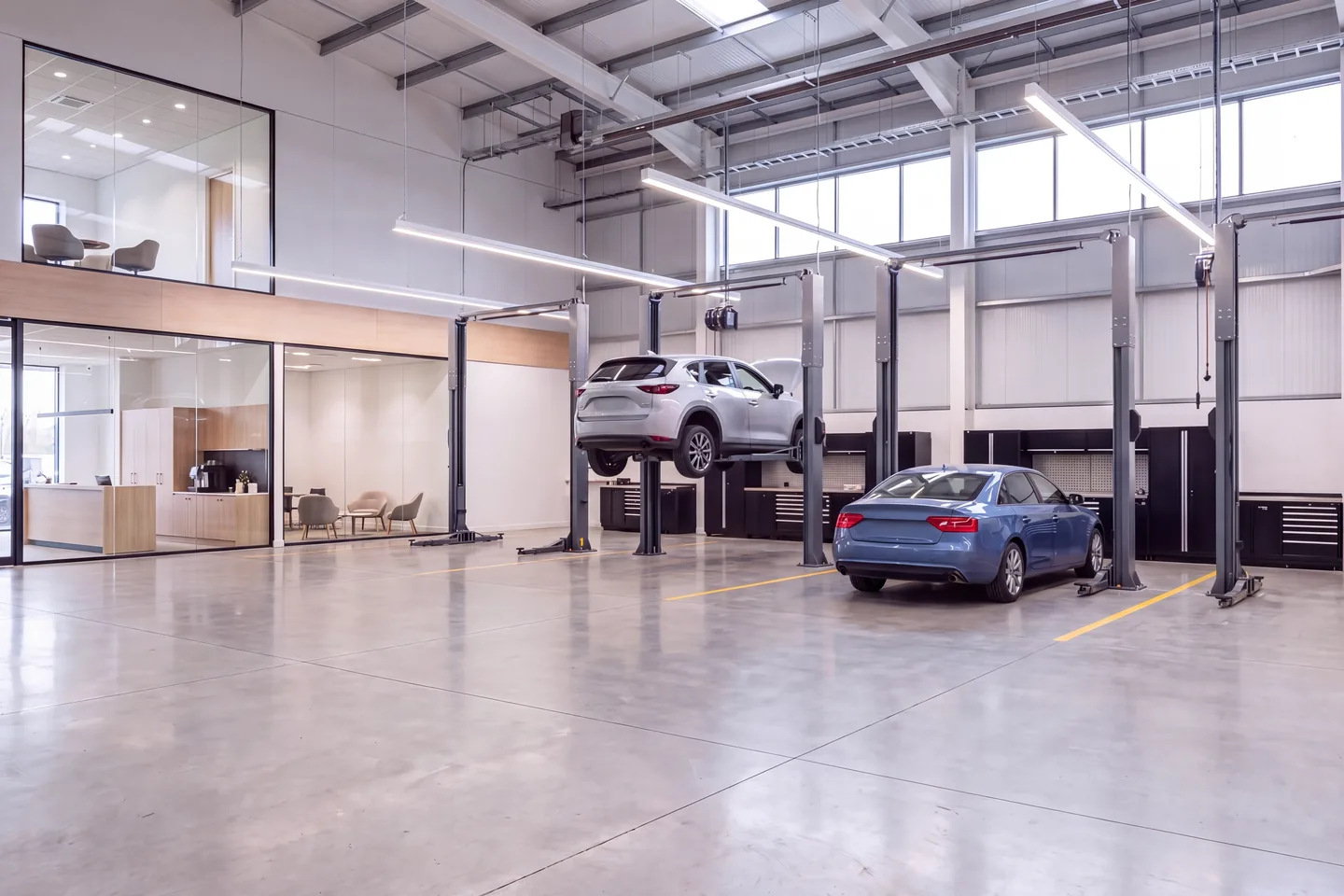 Render of a dealership service center with two-post lifts, a car raised on one bay and a glazed customer reception