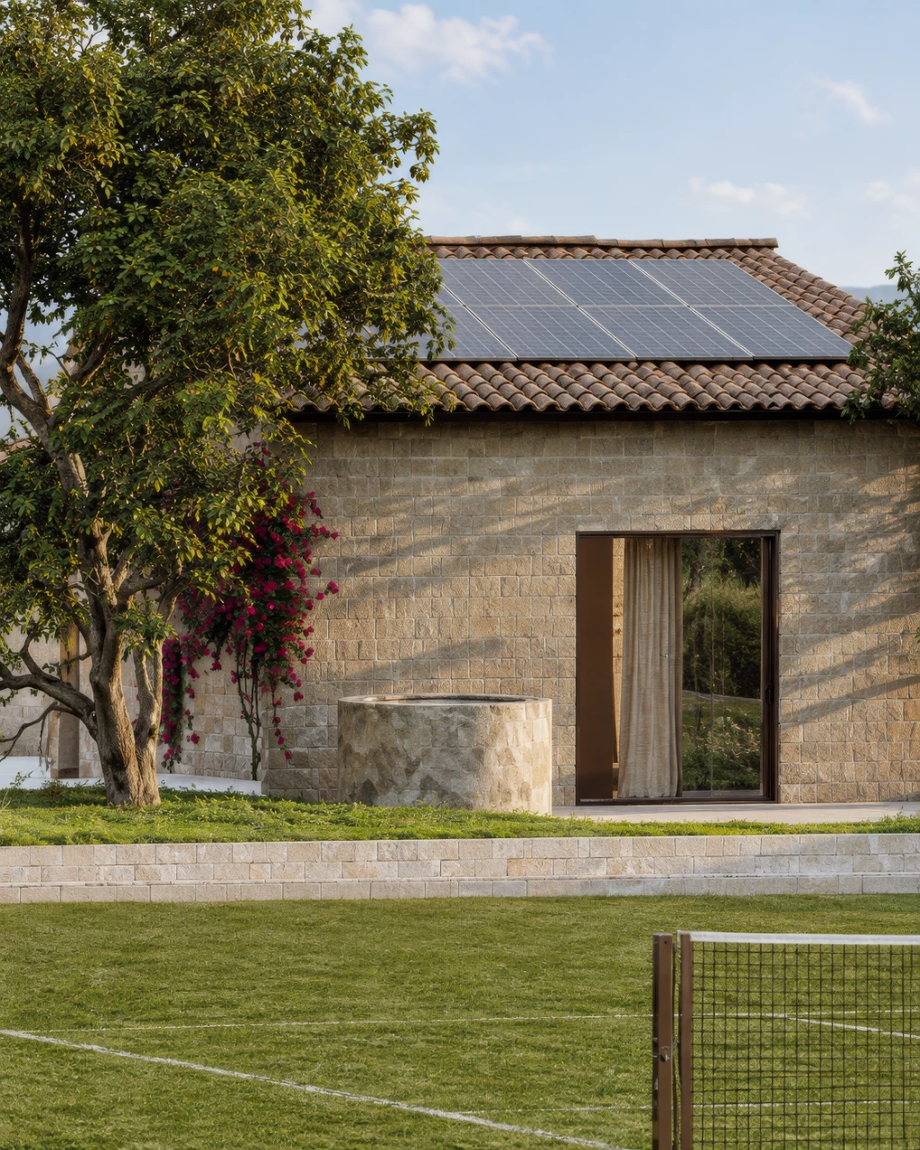 3D rendering of a modern stone house with solar panels, tree and garden, viewed from the side.