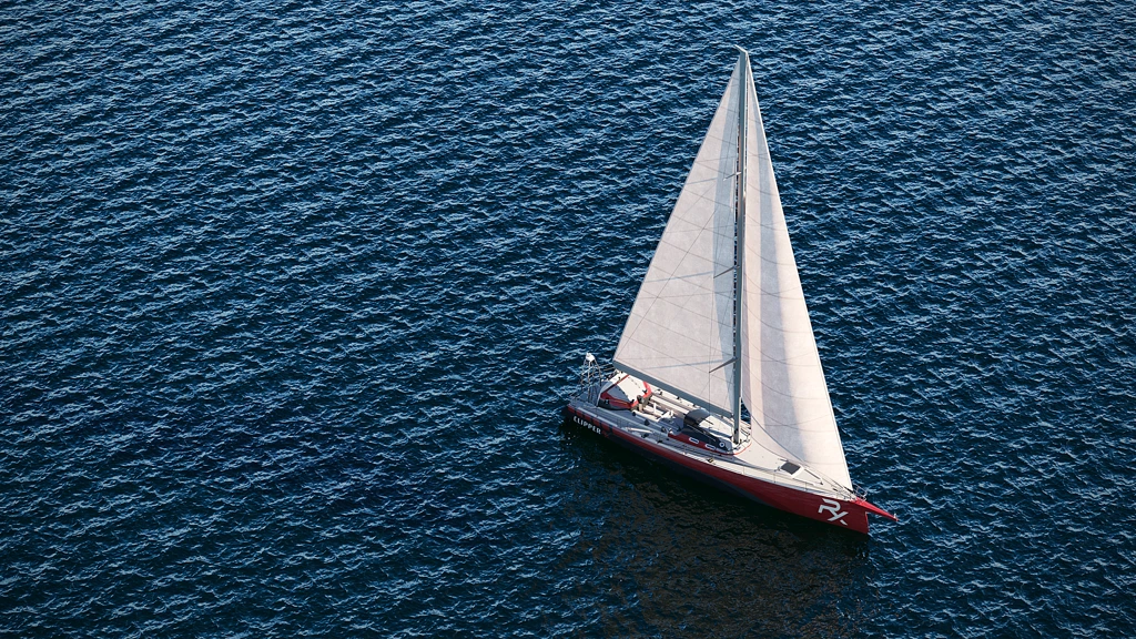 3D-Rendering eines roten Segelboots mit weißen Segeln auf dunkelblauem Wasser aus der Luft.