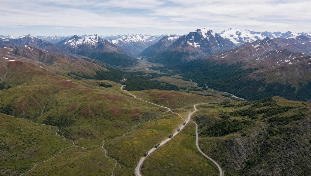 Convoy of expedition trucks on a winding road through a green mountain valley