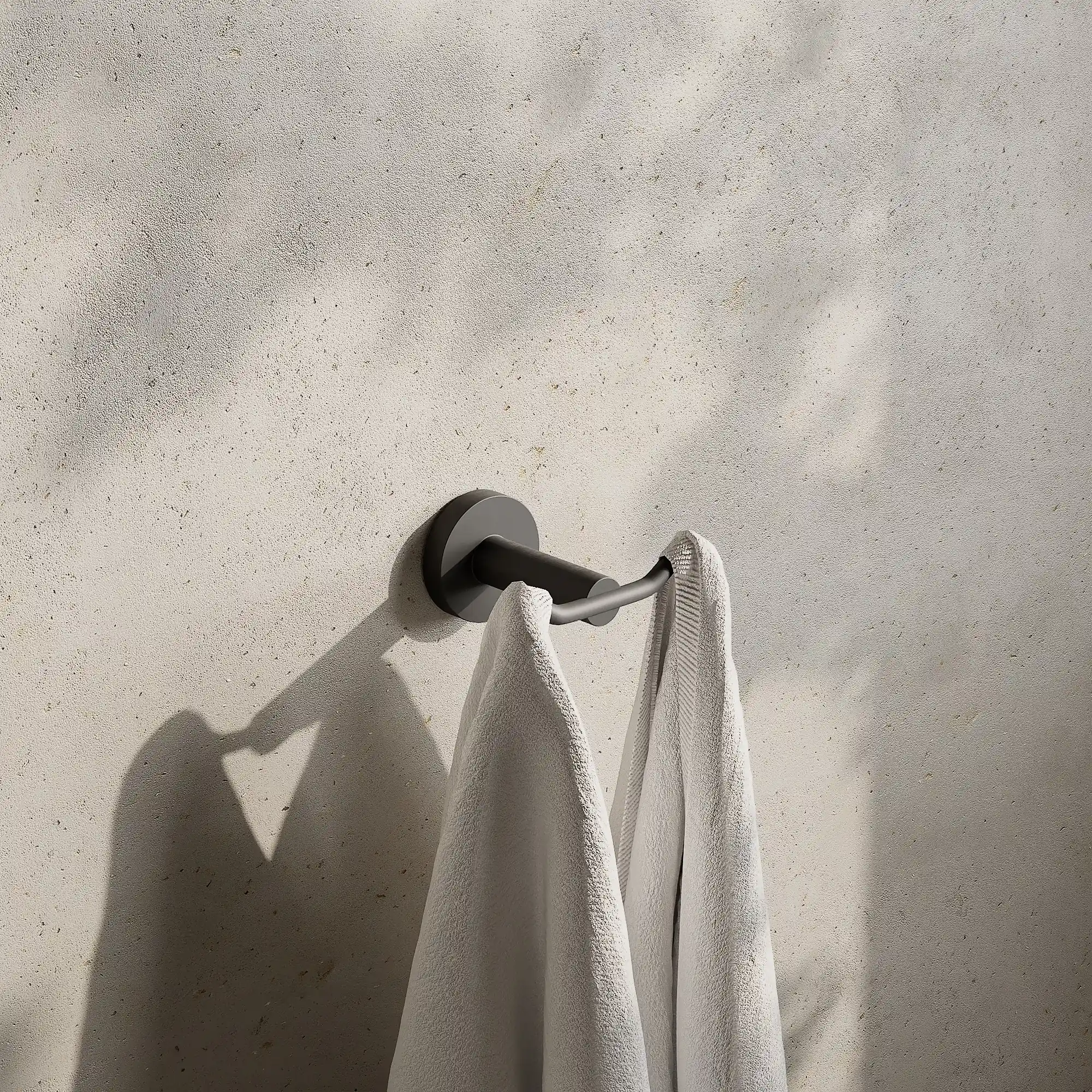 Render of a double robe hook in gunmetal black with two white towels on a stone wall