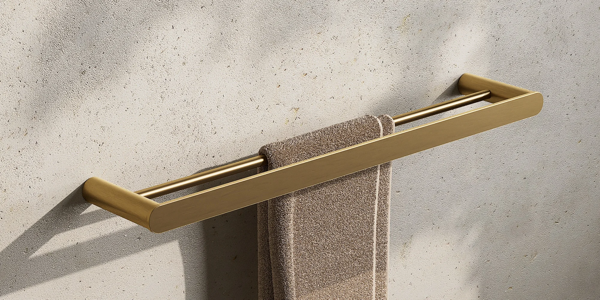 Render of a double towel rail in brushed gold with a beige hand towel on a warm stone wall with leaf shadows