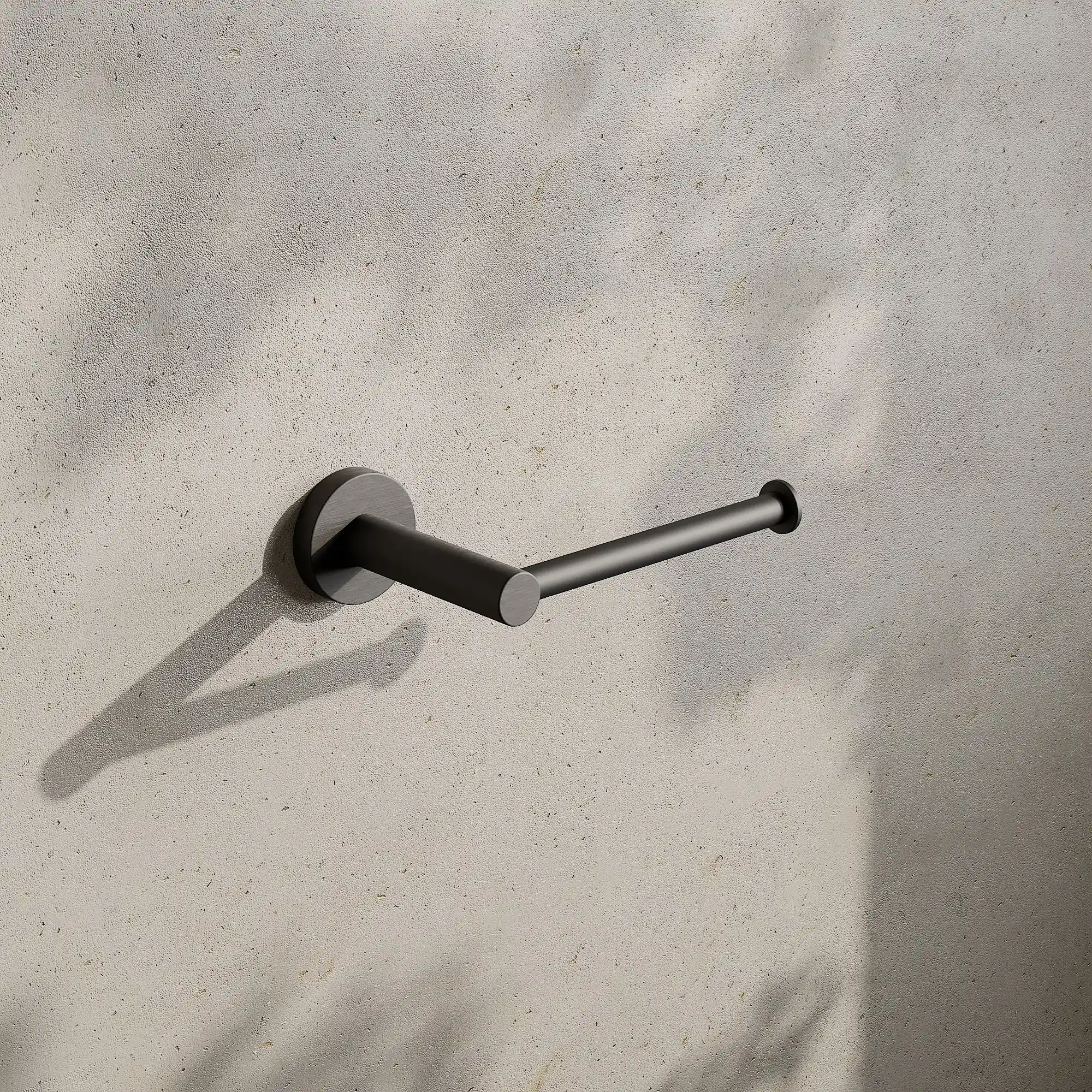 Render of a toilet roll holder in gunmetal black on a stone wall with leaf shadows