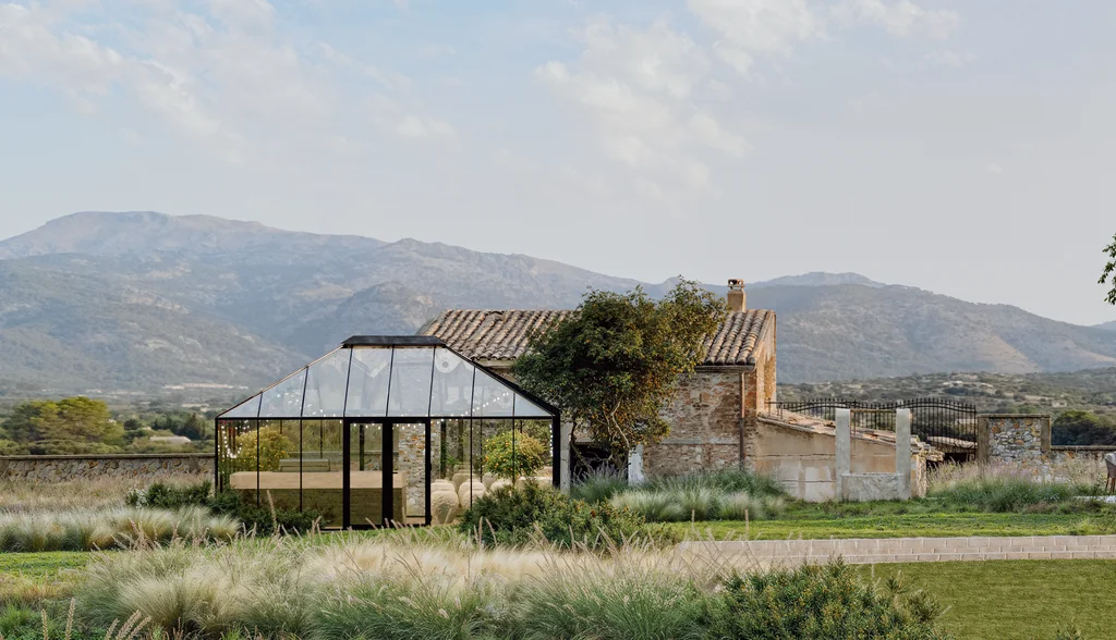 Render of a glasshouse beside a renovated stone barn across meadow planting, with mountains behind