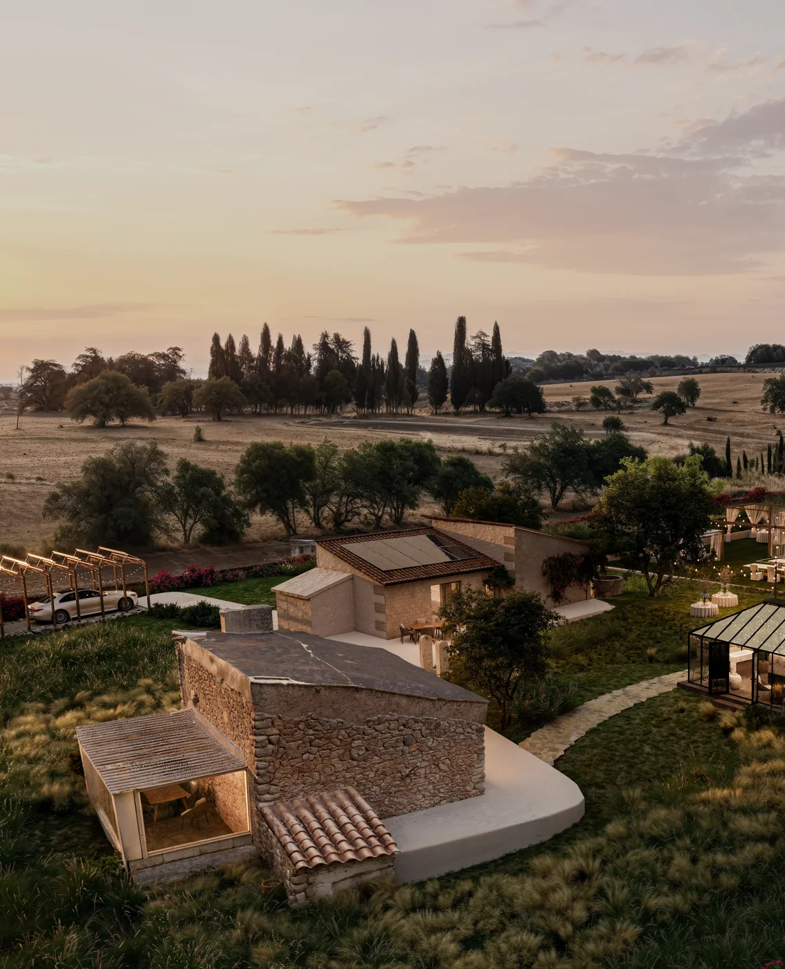 Sunset aerial render of a stone cottage, glasshouse and lawn set for an evening reception on a Mallorca finca