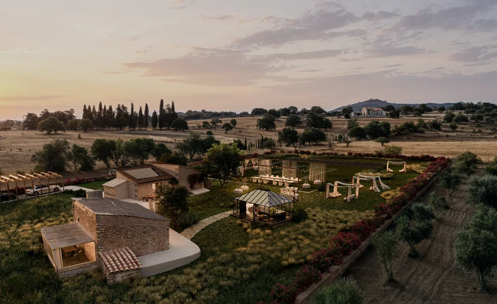 Sunset aerial render of a renovated finca lawn set for an evening reception with white drapes and string lights