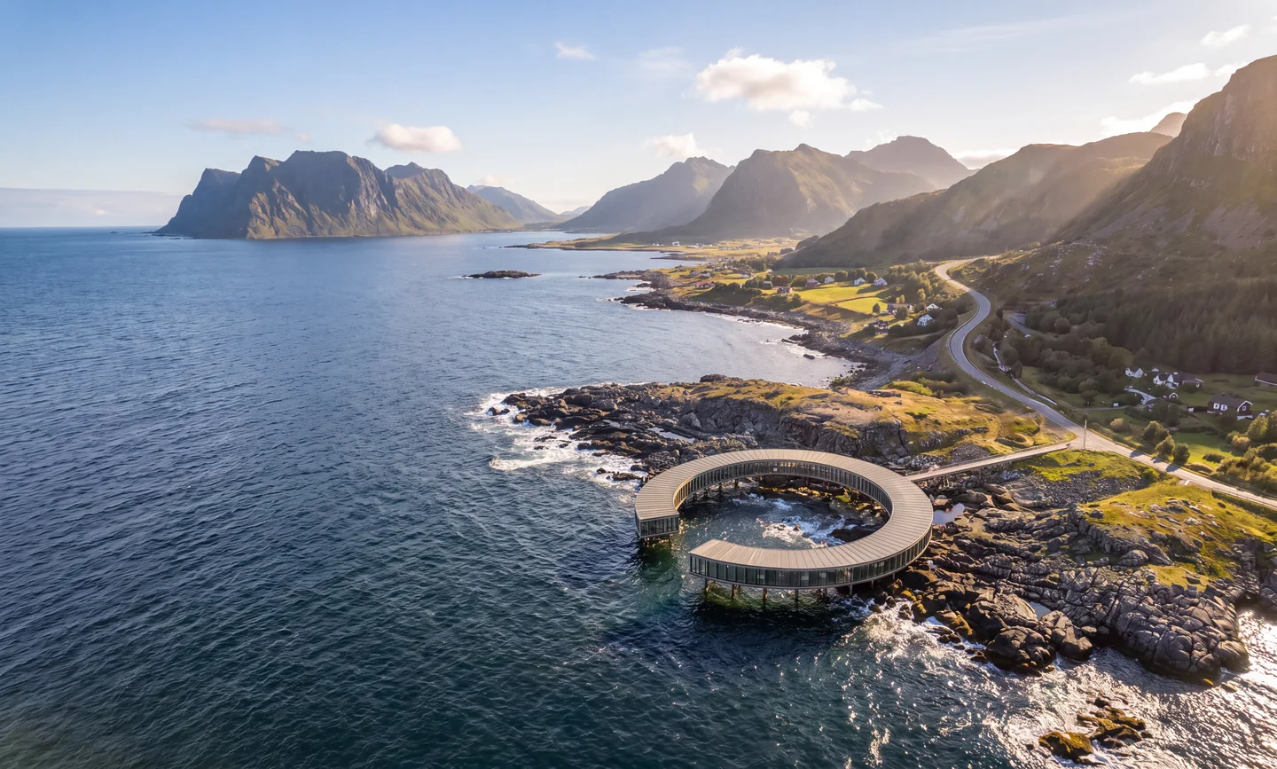 Aerial render of the open ring over a tidal pool on the rocky Lofoten coast, with mountains and a winding road in low sun