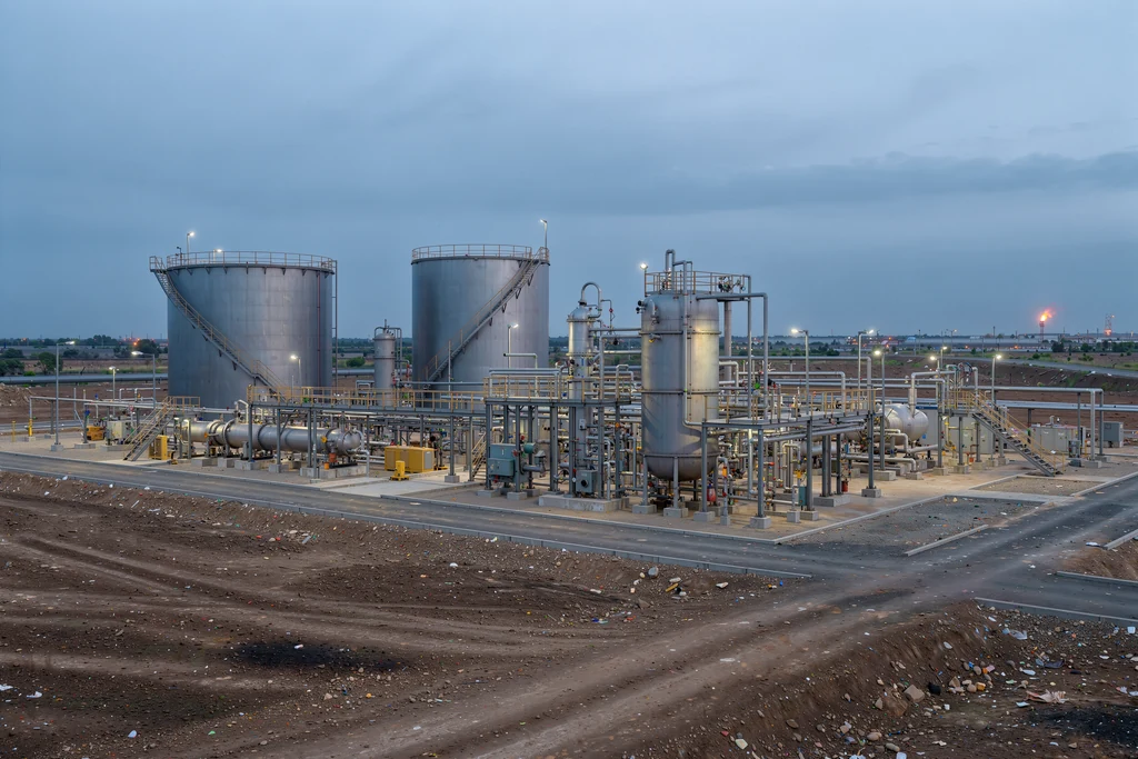 Oil and gas processing facility with storage tanks and piping at dusk