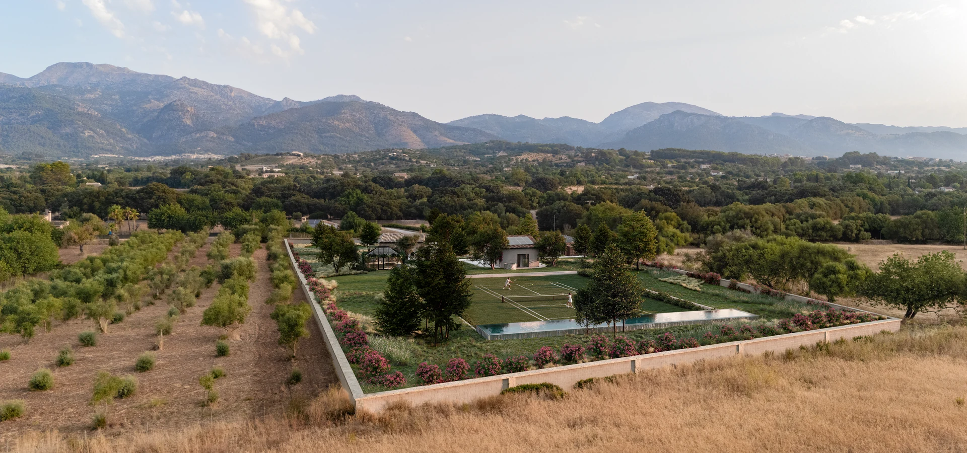 Drone aerial render of a renovated Mallorca finca with a walled garden, grass tennis court and raised pool below the mountains
