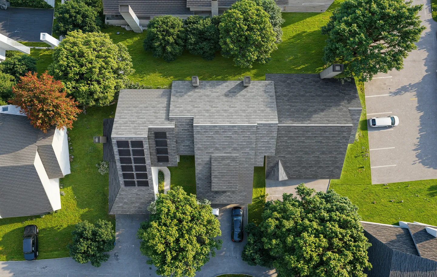 Aerial render of a townhouse community with a solar-equipped roof, lawns, trees and a parking area