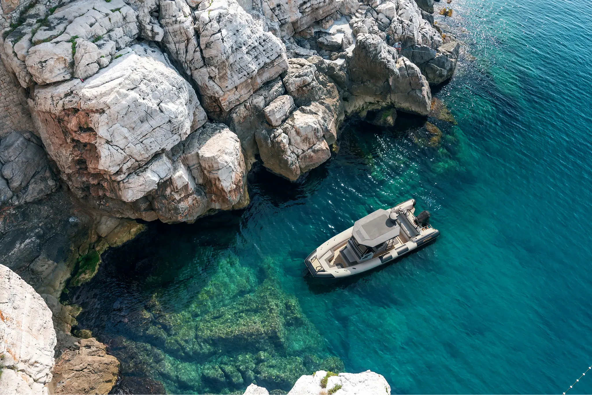 Compact motor yacht navigating near steep coastal rocks in clear turquoise sea