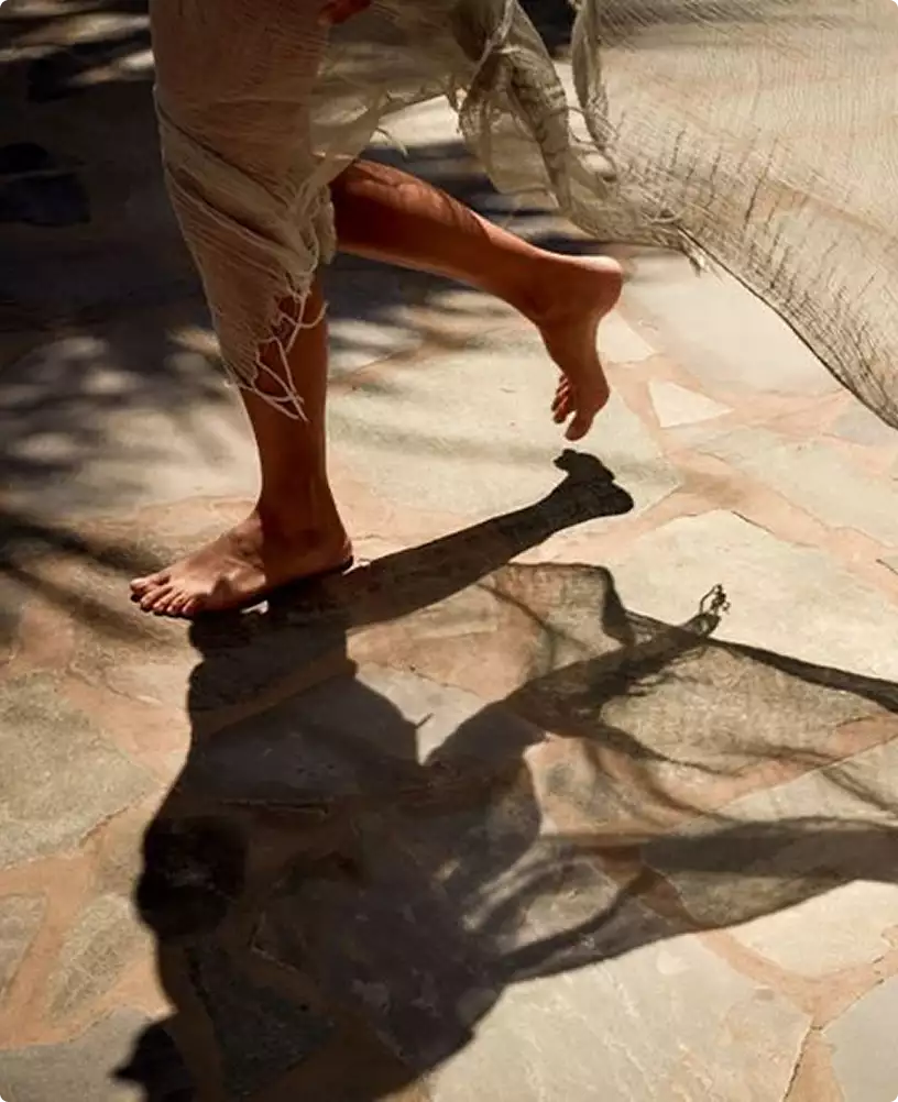 Eco houses design lifestyle scene with barefoot person walking on sunlit stone floor and flowing fabric shadow