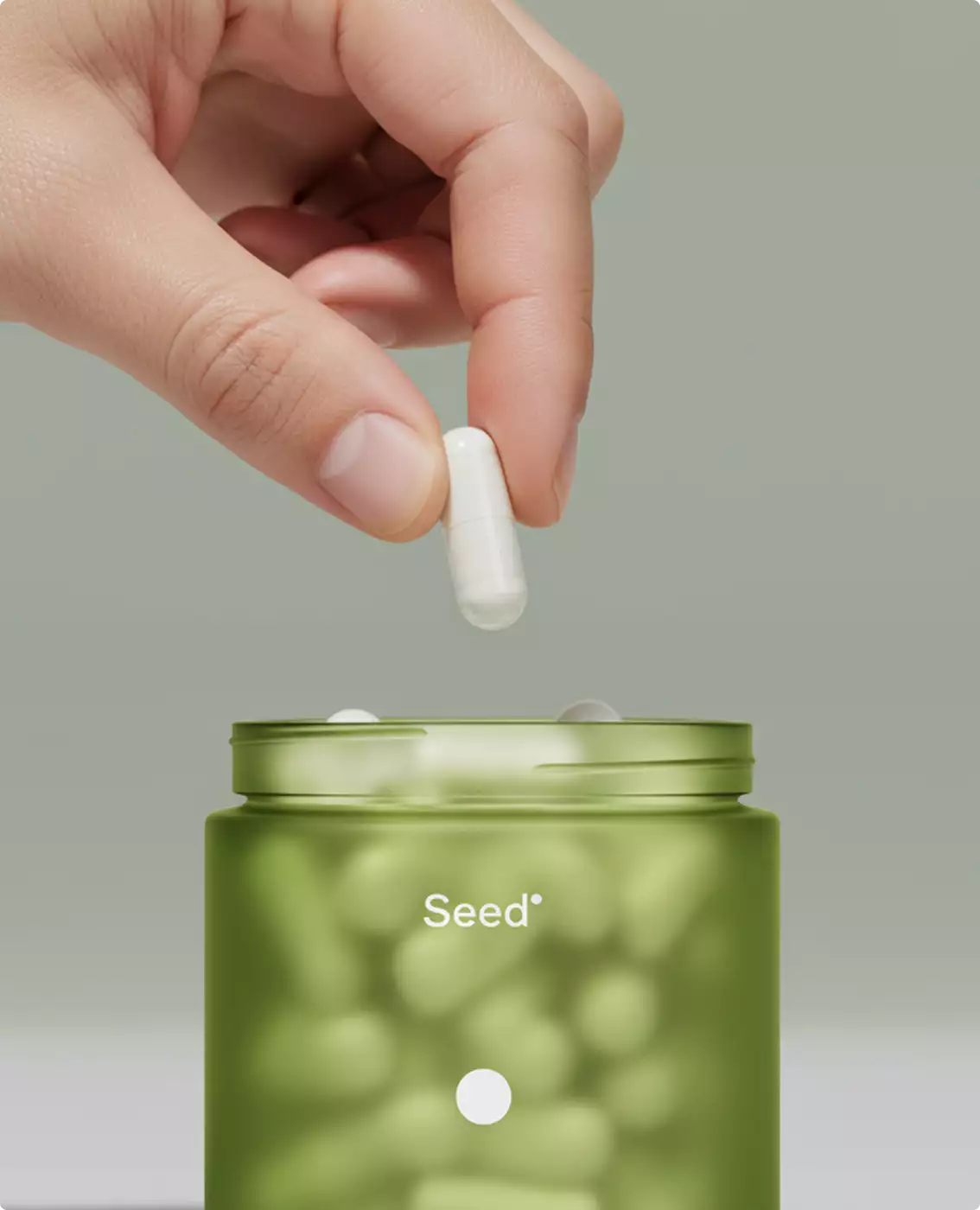Hand placing white capsule into green Seed supplement jar, supplement packaging design