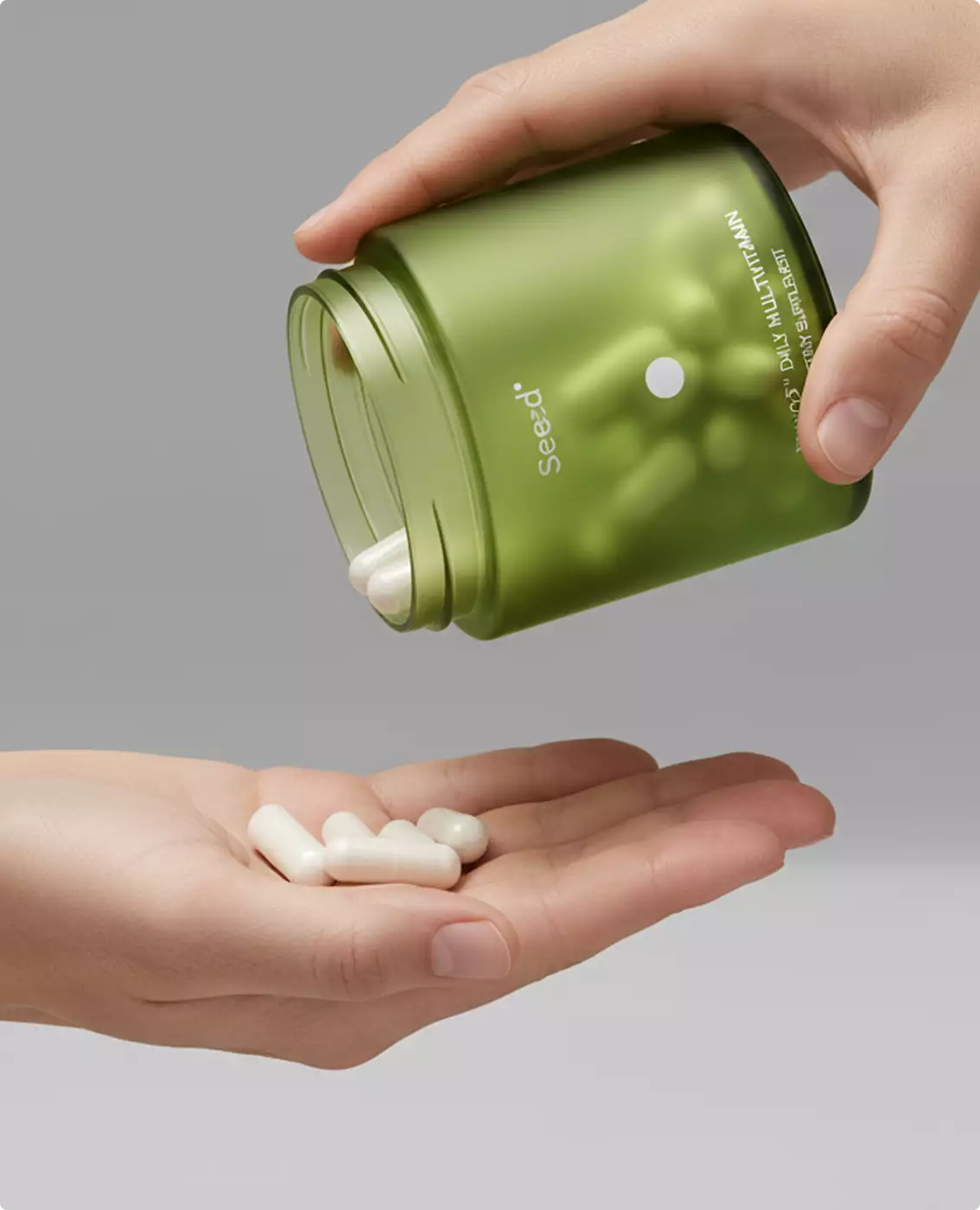 White capsules pouring from green Seed jar into open hand on neutral background, supplement packaging design