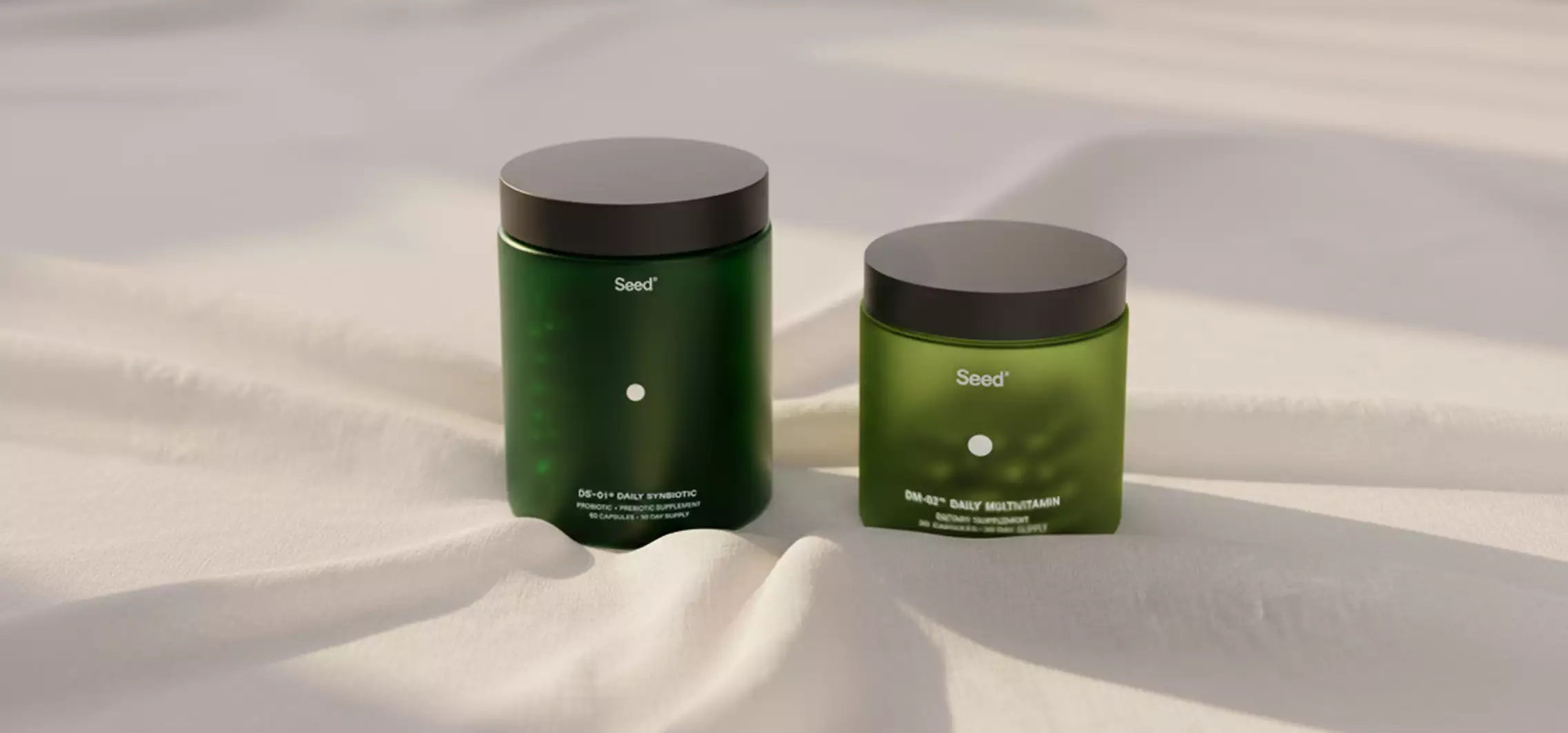 Two green Seed supplement jars on soft white fabric background, supplement packaging design
