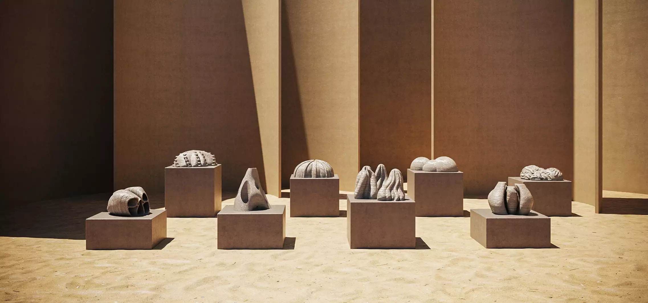 Multiple abstract stone sculptures on square pedestals in sandy courtyard with tall walls, display for 3D product renderings