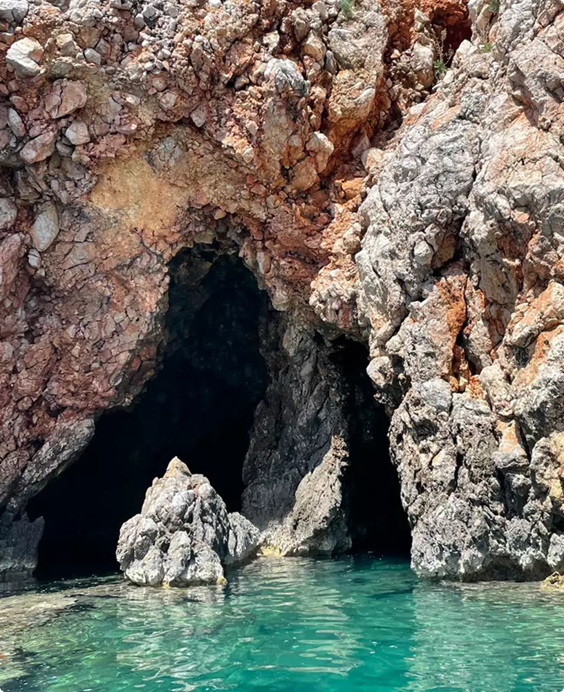Rocky sea cave opening in coastal cliff above turquoise water, natural formation resembling shapes used in 3D product renderings